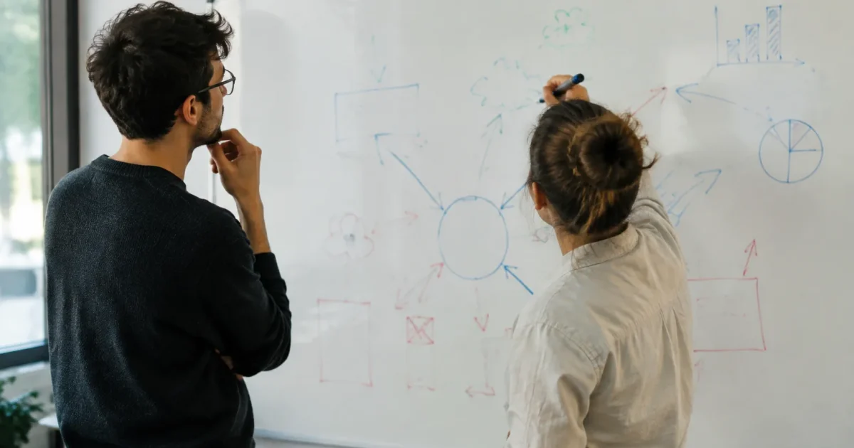 Deux personnes debout devant un tableau blanc annoté