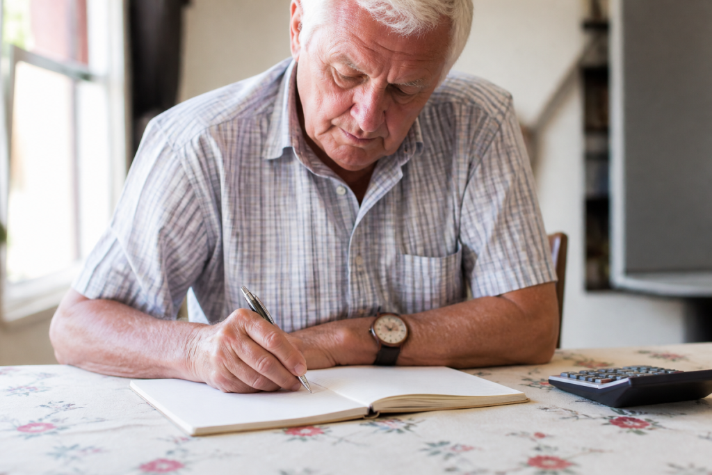 Homme senior notant des chiffres sur un carnet ouvert