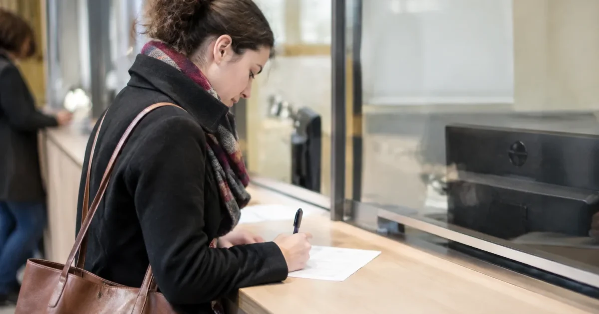 Une personne debout remplit un formulaire papier au guichet
