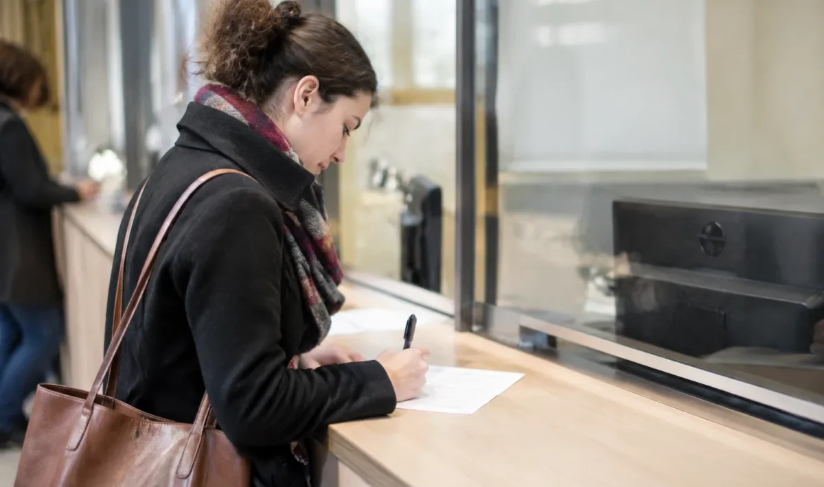 Une personne debout remplit un formulaire papier au guichet